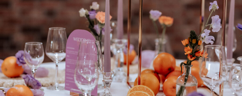 Tischdekoration mit Orangen, lila Kerzen und Tischnummer 1