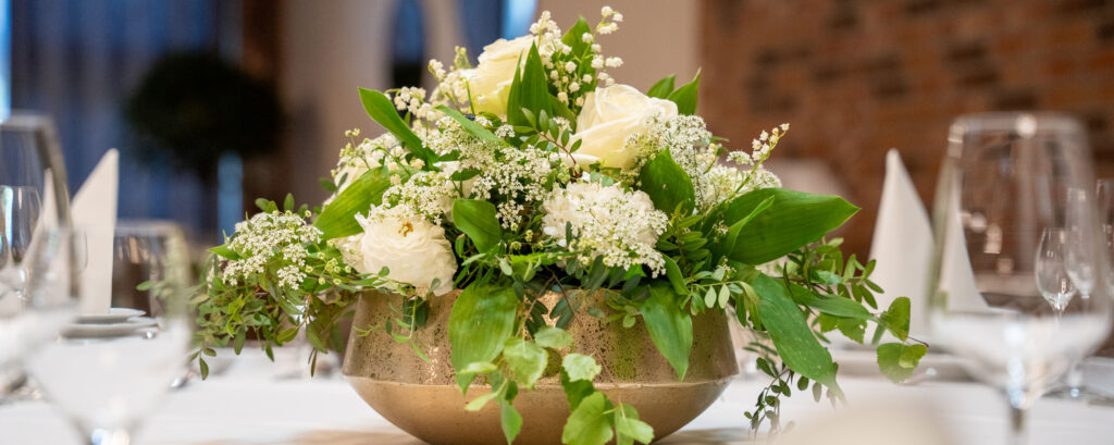 Weißer Blumenstrauß in goldener Schale auf Tisch